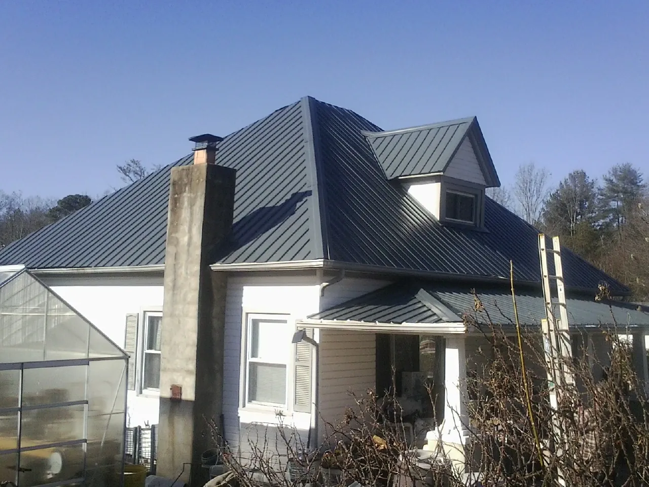 Dark blue standing seam metal roof on a white farmhouse with dormer — Slate & Tile Roof Repair by Roofing Brothers in Notus