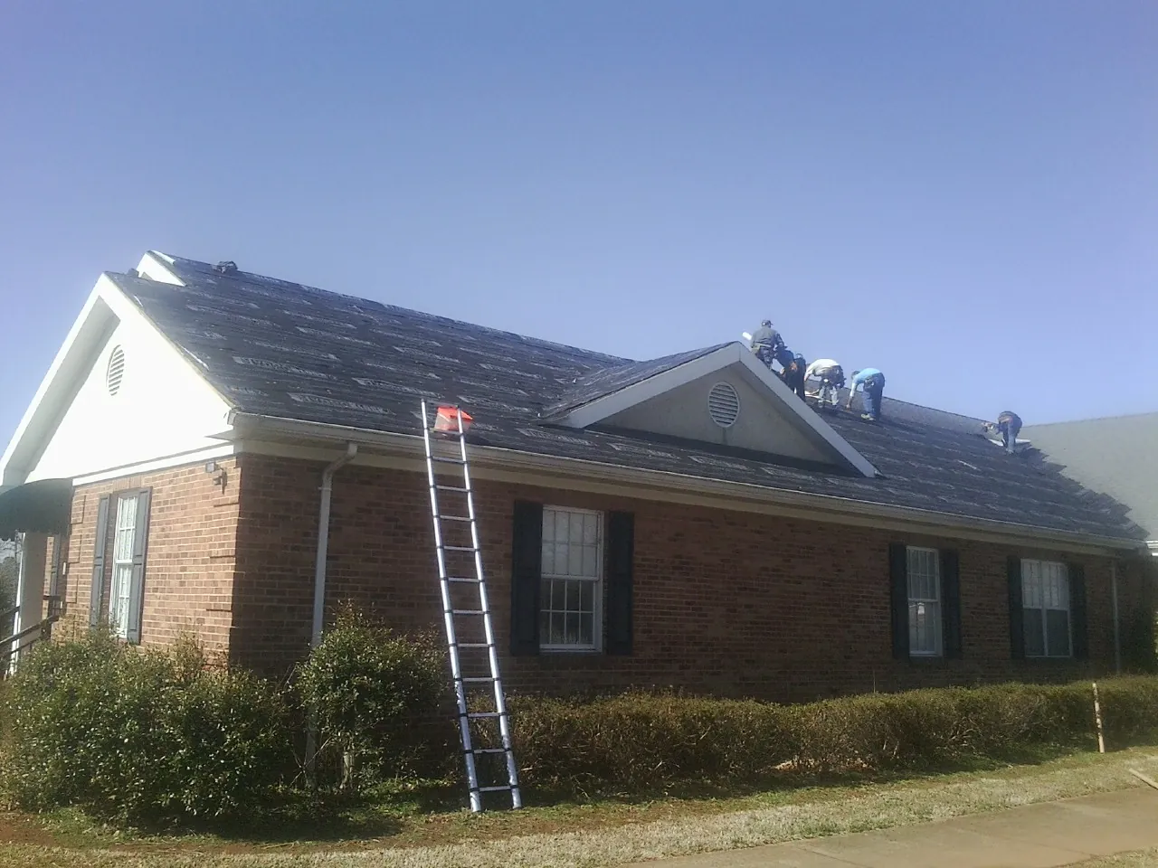 Crew tearing shingles off a brick ranch roof with a ladder set — Emergency Roof Repair work by our crew in Notus