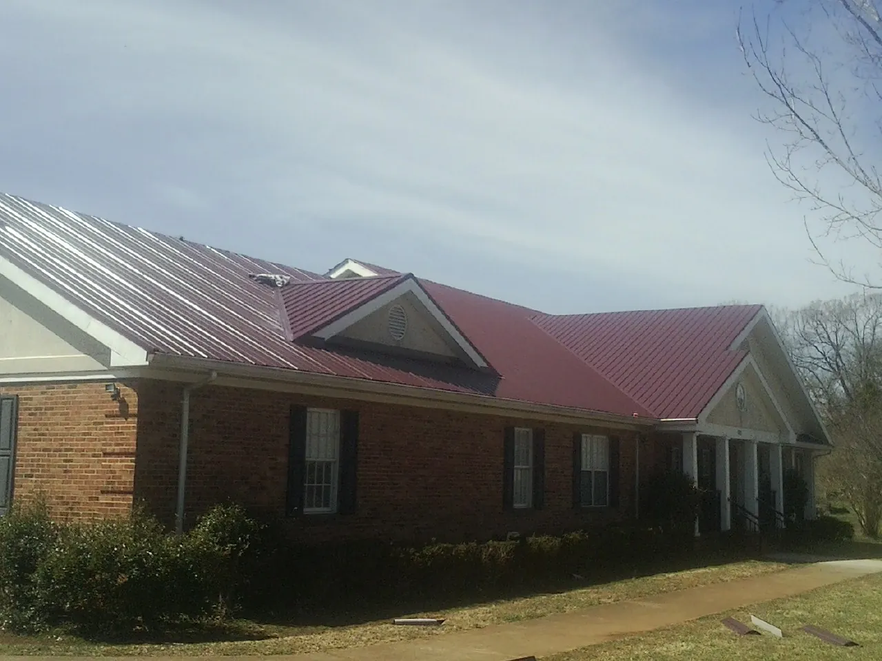 Red metal roof with gabled entries on a long brick building, from a Hail Damage Roof Repair job in Notus