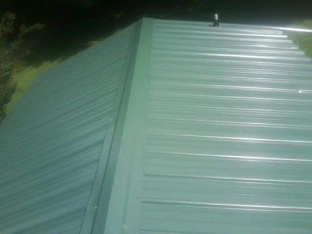 New green metal panels meeting at the ridge of a roof — Flat Roof Repair work by our crew in Notus