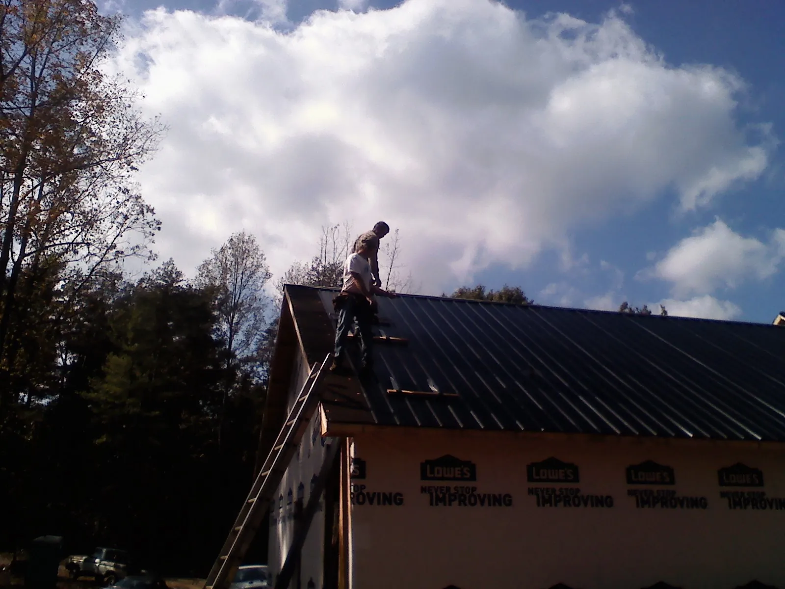 Roofer fastening dark metal panels high against a cloudy sky, from a Roof Inspection job in Notus