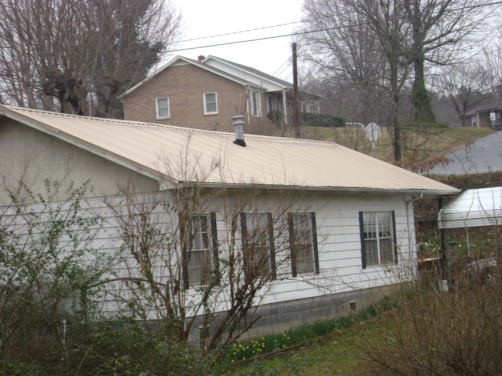 Tan metal roof on a white sided house set into a hillside — Commercial Roofing by Roofing Brothers in Notus